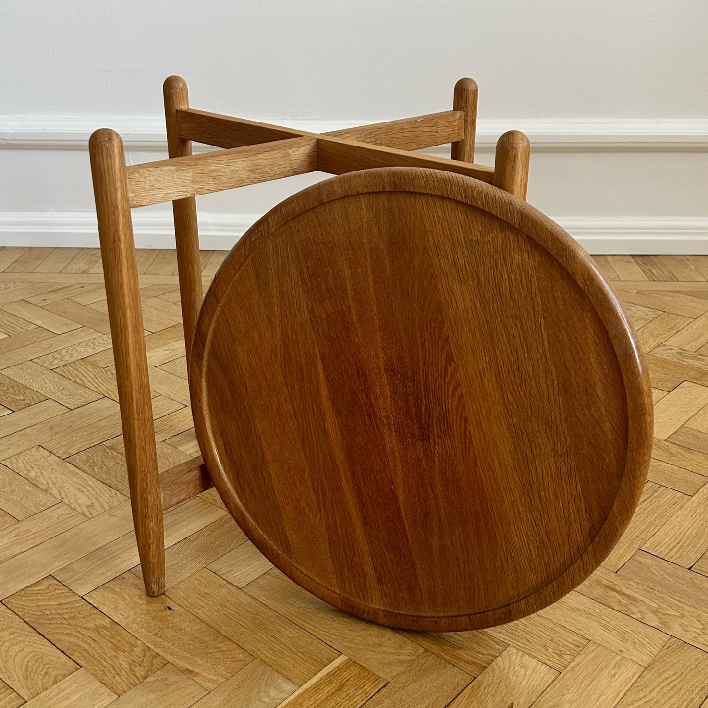 Wooden stool with round seat and open backrest on a wooden floor.