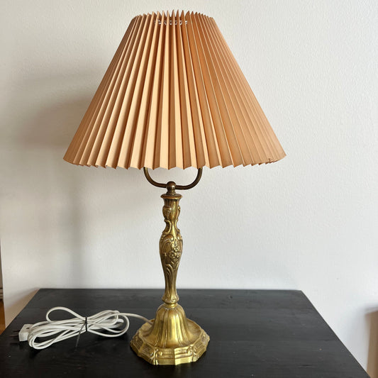 Brass table lamp with pleated beige shade on a dark surface
