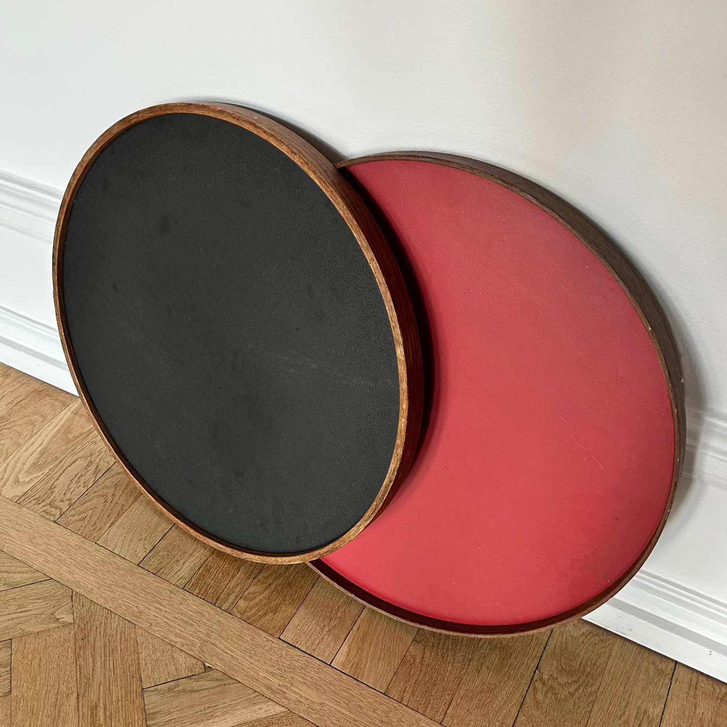 Two round stools, one black and one red, on a wooden floor with a white wall background.
