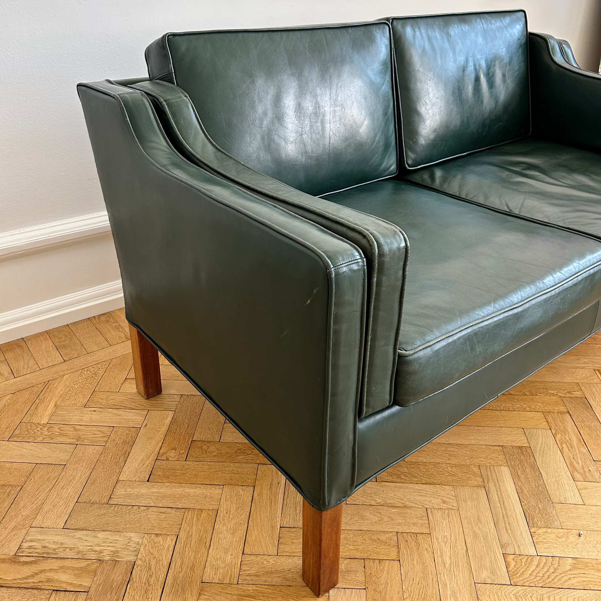 Green leather sofa on a wooden floor with a white wall background