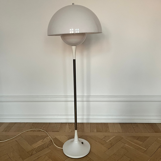Floor lamp with a white base and gray shade on a wooden floor against a white wall.
