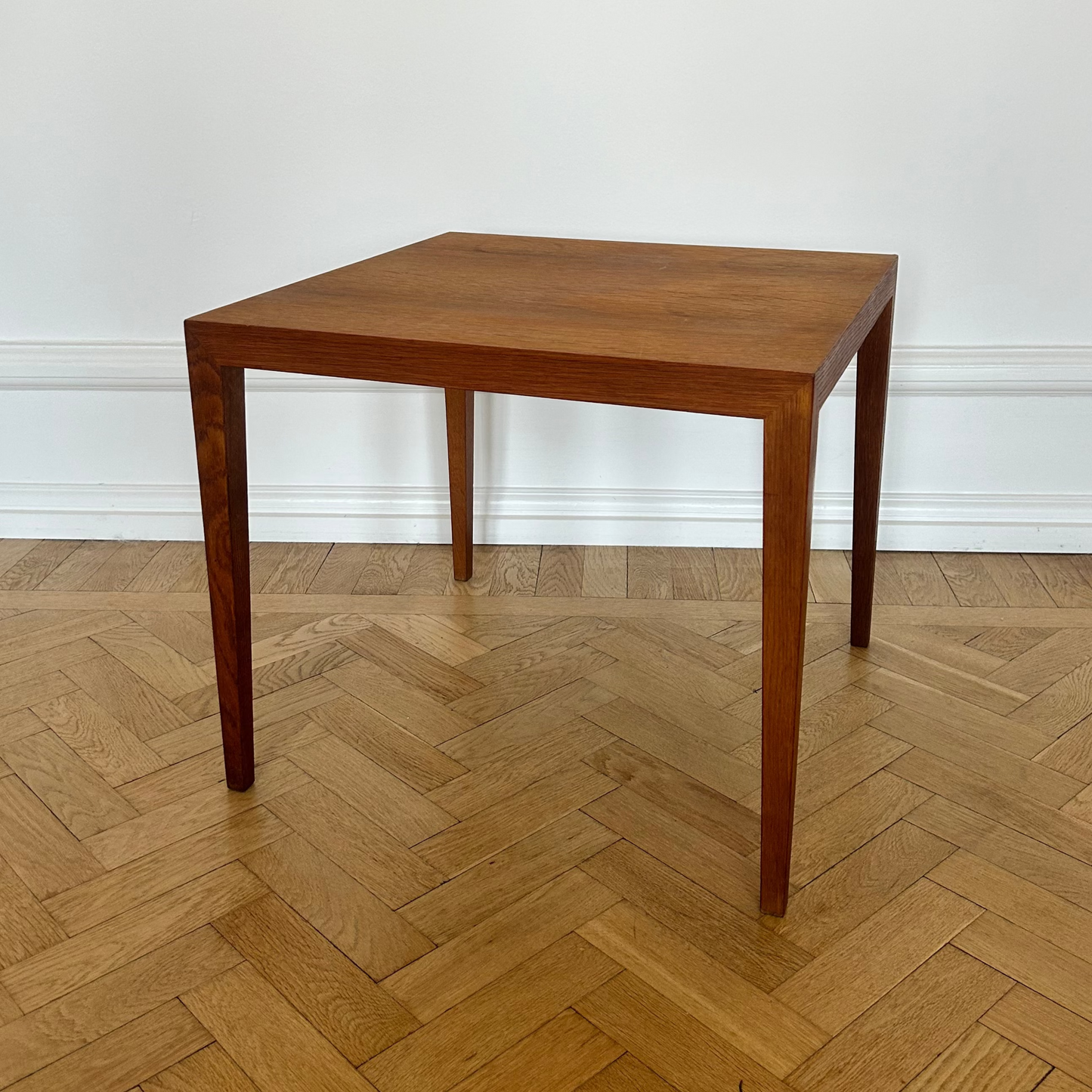 Wooden table on a herringbone wooden floor with a white wall background